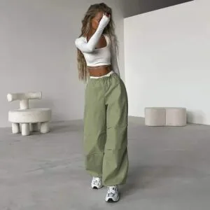 Femme élégante en crop top blanc et pantalon oversized vert dans un intérieur minimaliste.