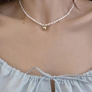 Collier En Perles Blanches Élégant Avec Charme Doré Sur Blouse Légère Bleuâtre.