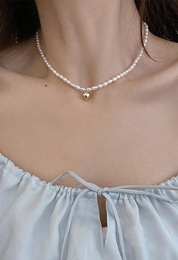 Collier En Perles Blanches Élégant Avec Charme Doré Sur Blouse Légère Bleuâtre.