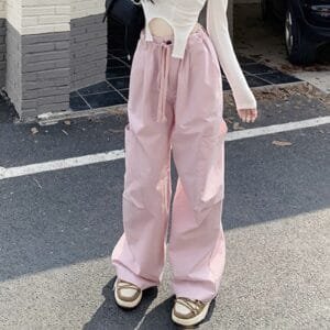 Pantalon large rose tendance avec top blanc et sneakers chunky, look décontracté en milieu urbain.