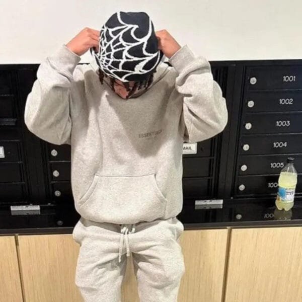 Jeune Avec Sweats Et Bonnet Araignée Devant Des Casiers Modernes, Preparation Décontractée.