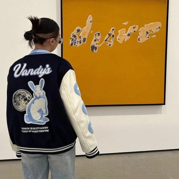 Jeune Observateur En Veste Varsity Admire Une Œuvre Dart Colorée Dans Une Galerie Moderne.